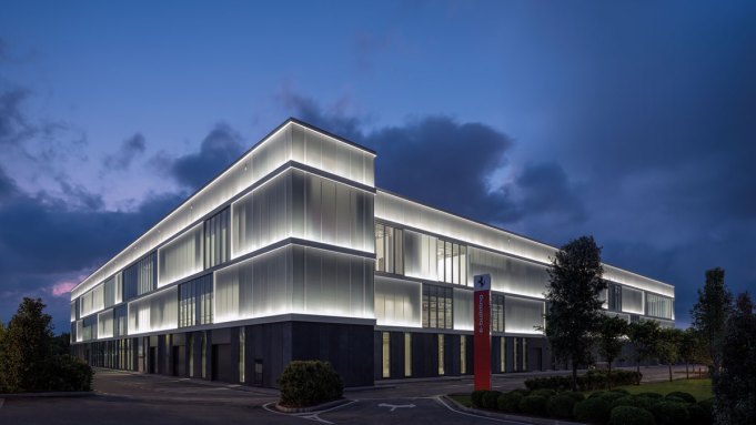 Ferrari 2024 年启用的 E-Building 工厂外观，现代化白色建筑群，侧面有巨大的 E-BUILDING 标识
