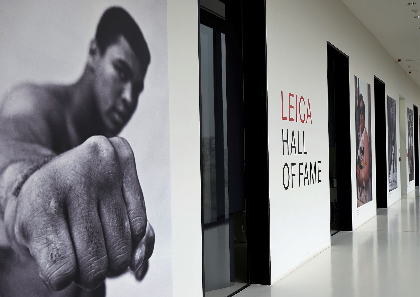 Leica Hall of Fame 展览空间，深色墙面上挂着大幅摄影师肖像，墙中央印有 LEICA HALL OF FAME 字样