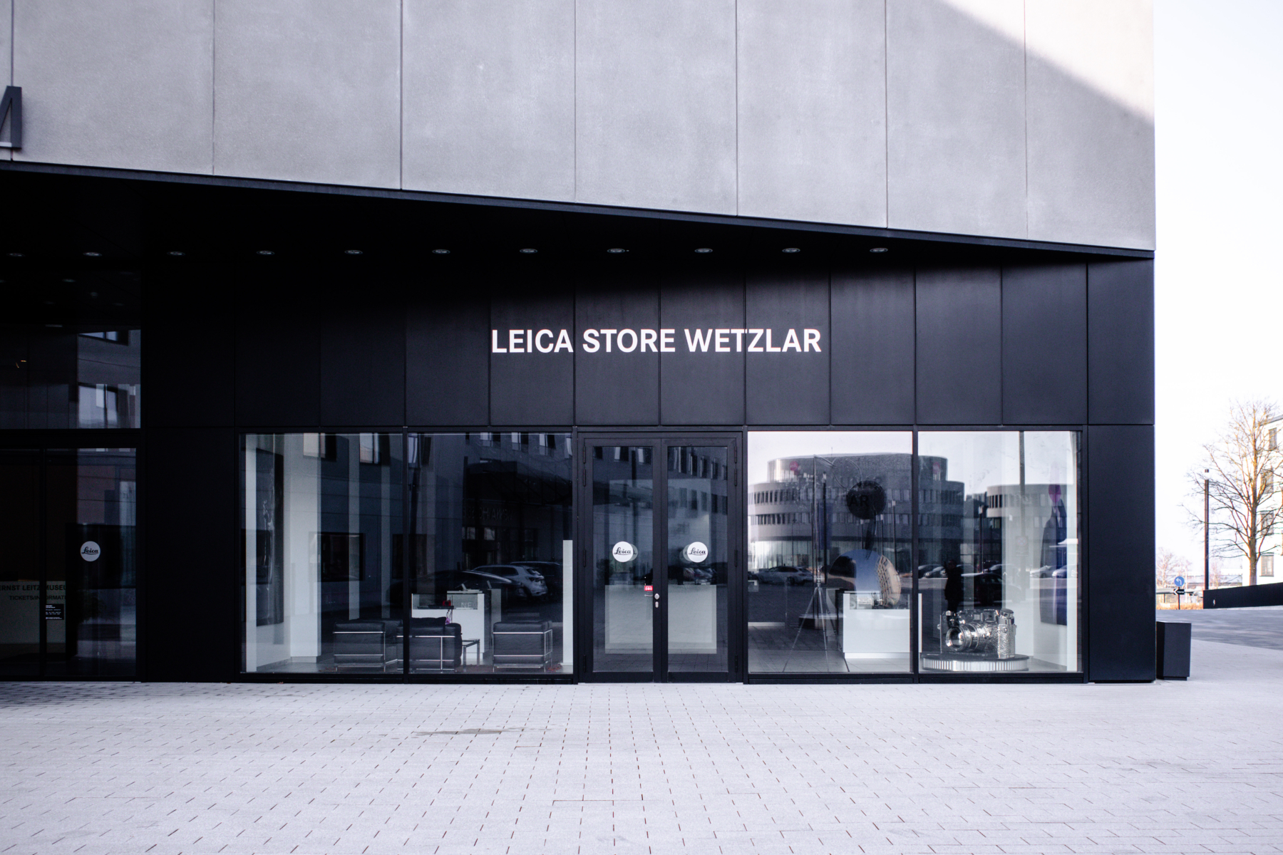 Leica Welt Wetzlar 旗舰店外观，现代黑色玻璃幕墙建筑，门前有露天咖啡座